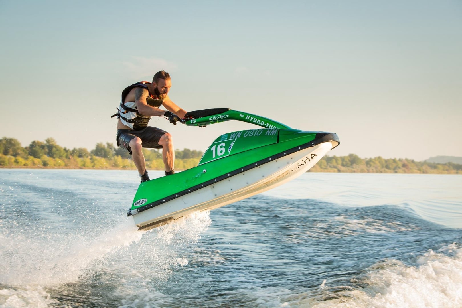 A man on a green jet ski jumping a wave in ocean