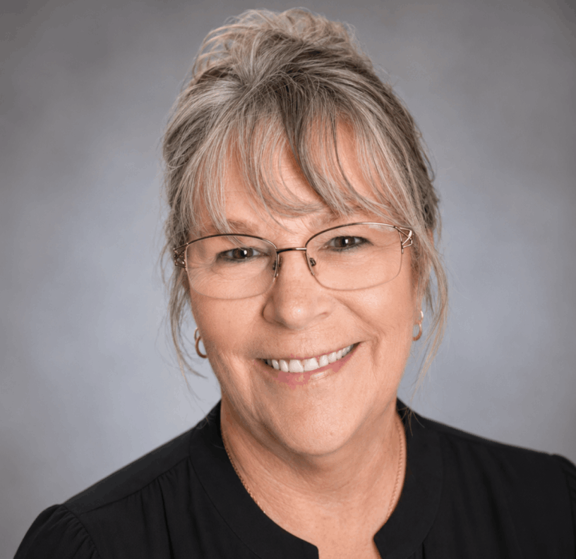 Judy McMahan wearing a black shirt and glasses with grey background